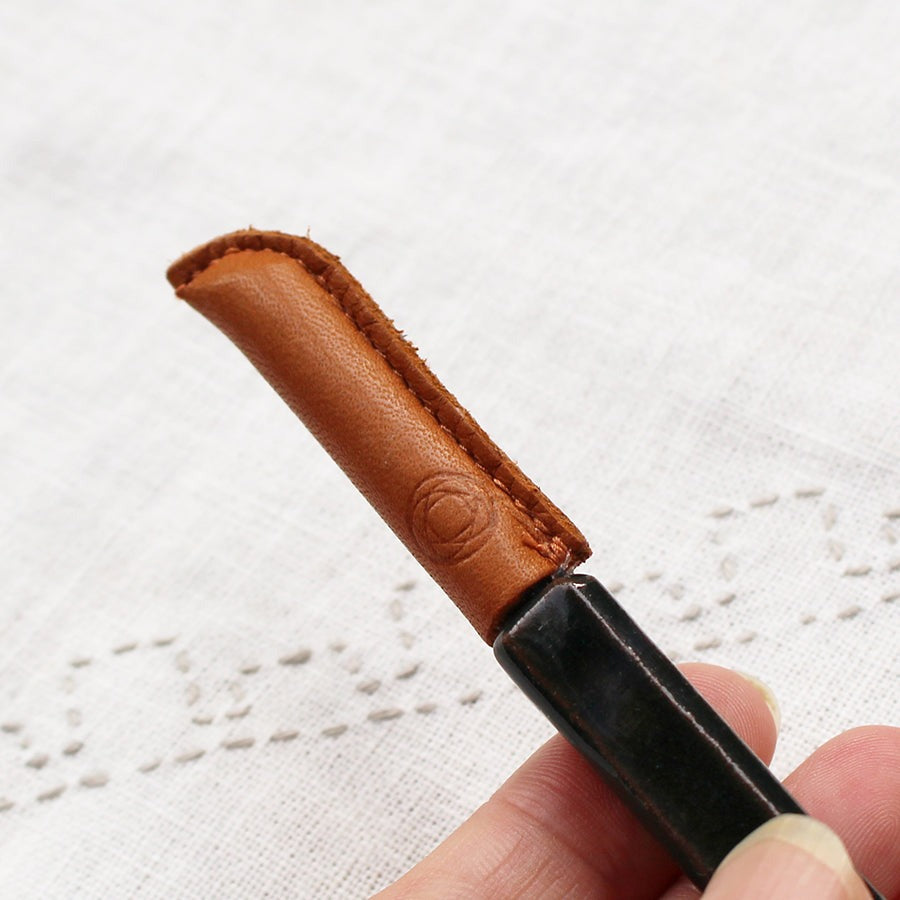 Close up of stitched brown leather case covering tip of seam ripper