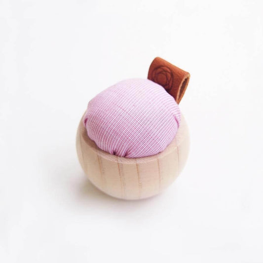 Small pincushion with pale wooden base, pink cushion and leather tag against white background