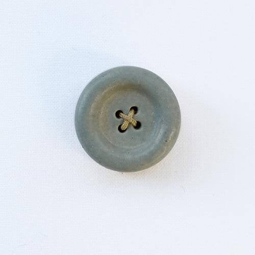 Grey ceramic button shaped needle holder on white background