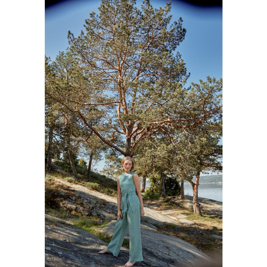 White woman standing in front of a tree wearing a green sleevless jumpsuit