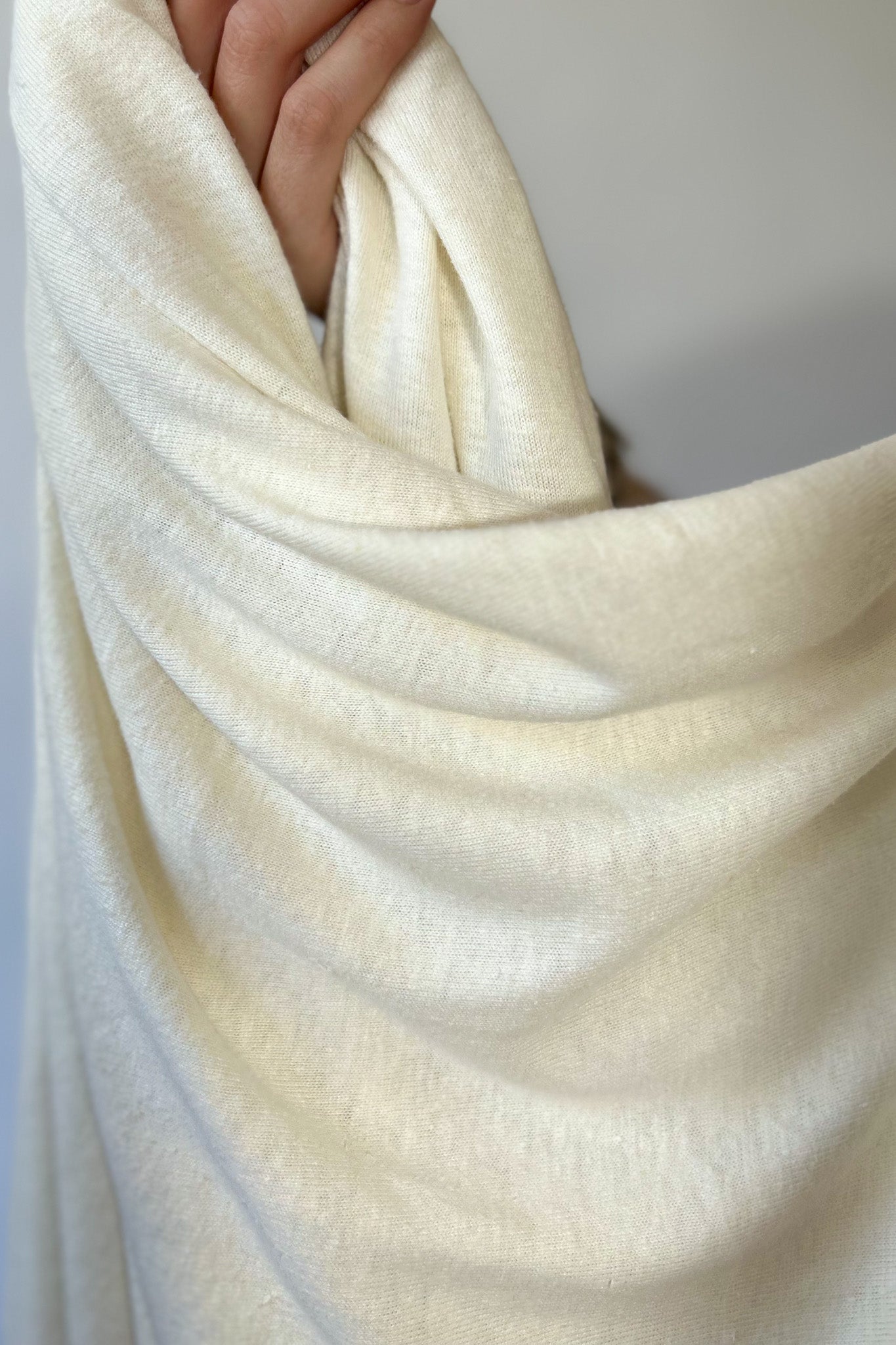 Close up of hand holding natural white coloured hemp and lyocell jersey knit fabric