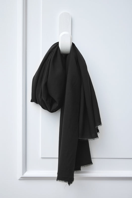 Piece of black Vida voile tencel sewing fabric handing on white hook