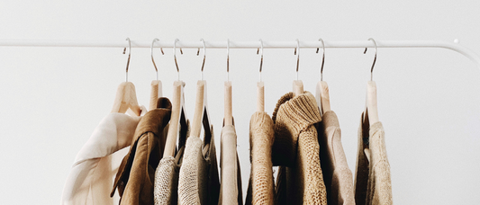 Row of beige clothes hanging on clothing rack with white background
