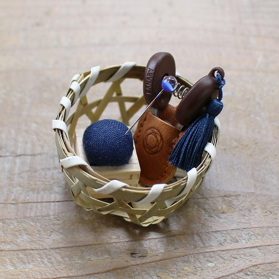 Small woven basket holding mini scissors with blue tassel and small blue wooden pin cushion with a blue pin