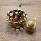 Small woven basket holding mini scissors with yellow tassel and small wooden based pin cushion with yellow fabric beside it on a wooden table