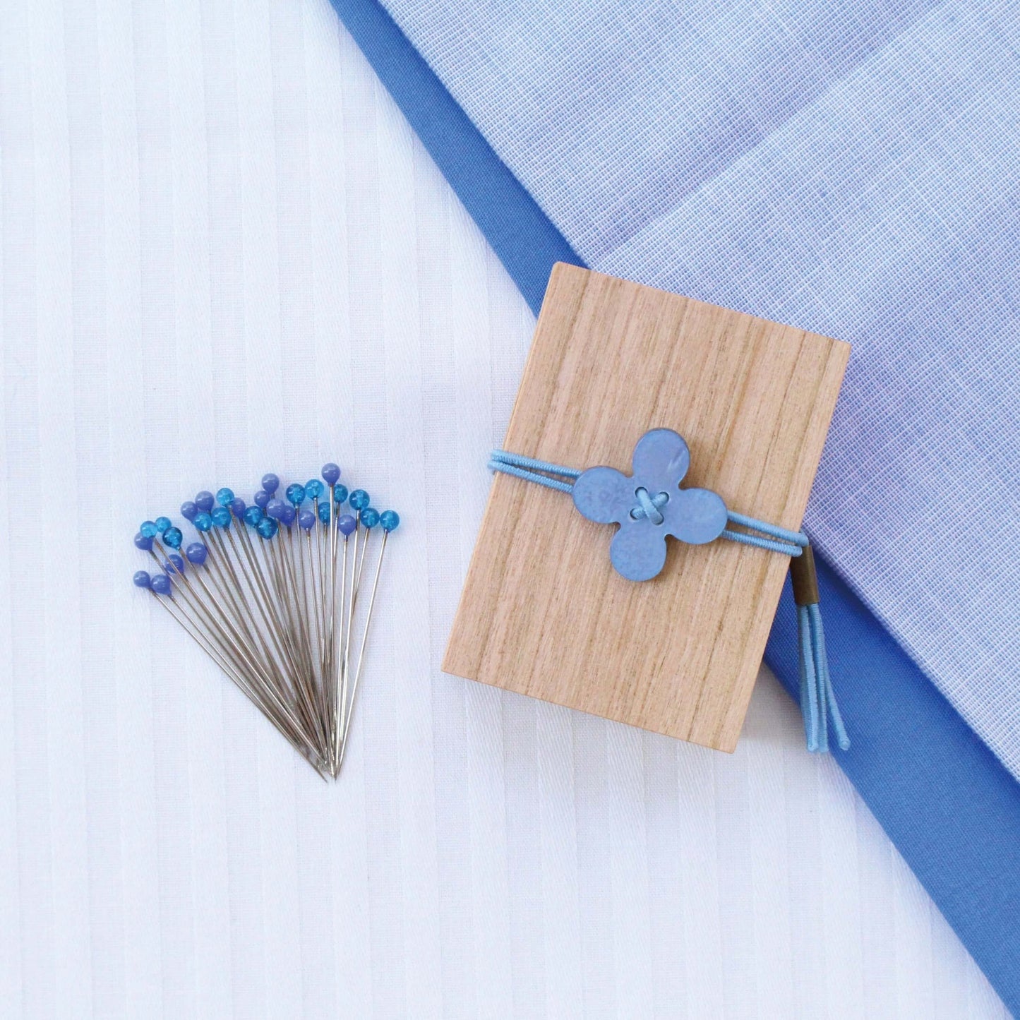 Cohana pins with blue glass heads sitting alongside wooden container with blue flower shell toggle