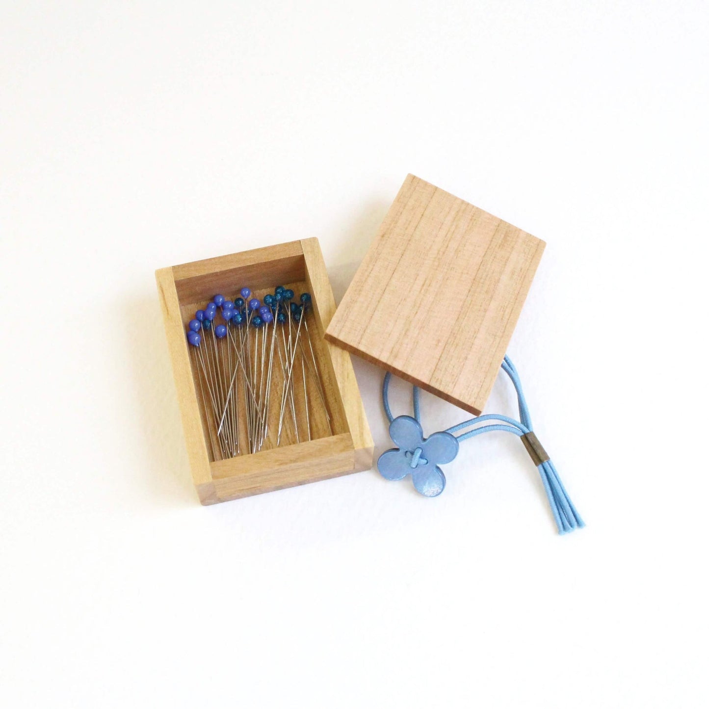 Open wooden box of blue glass headed pins by cohana