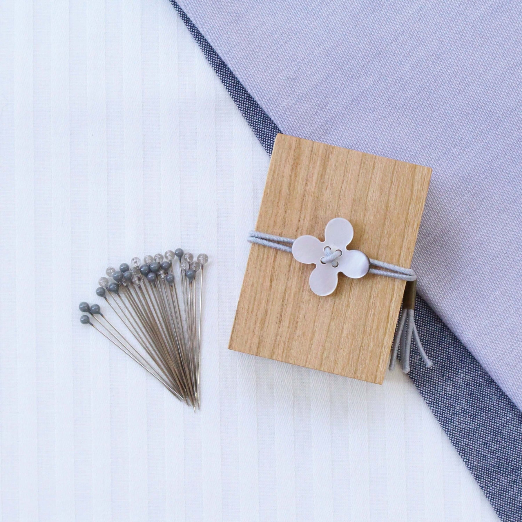 Grey glass headed pins along side wooden box with grey flower shell toggle