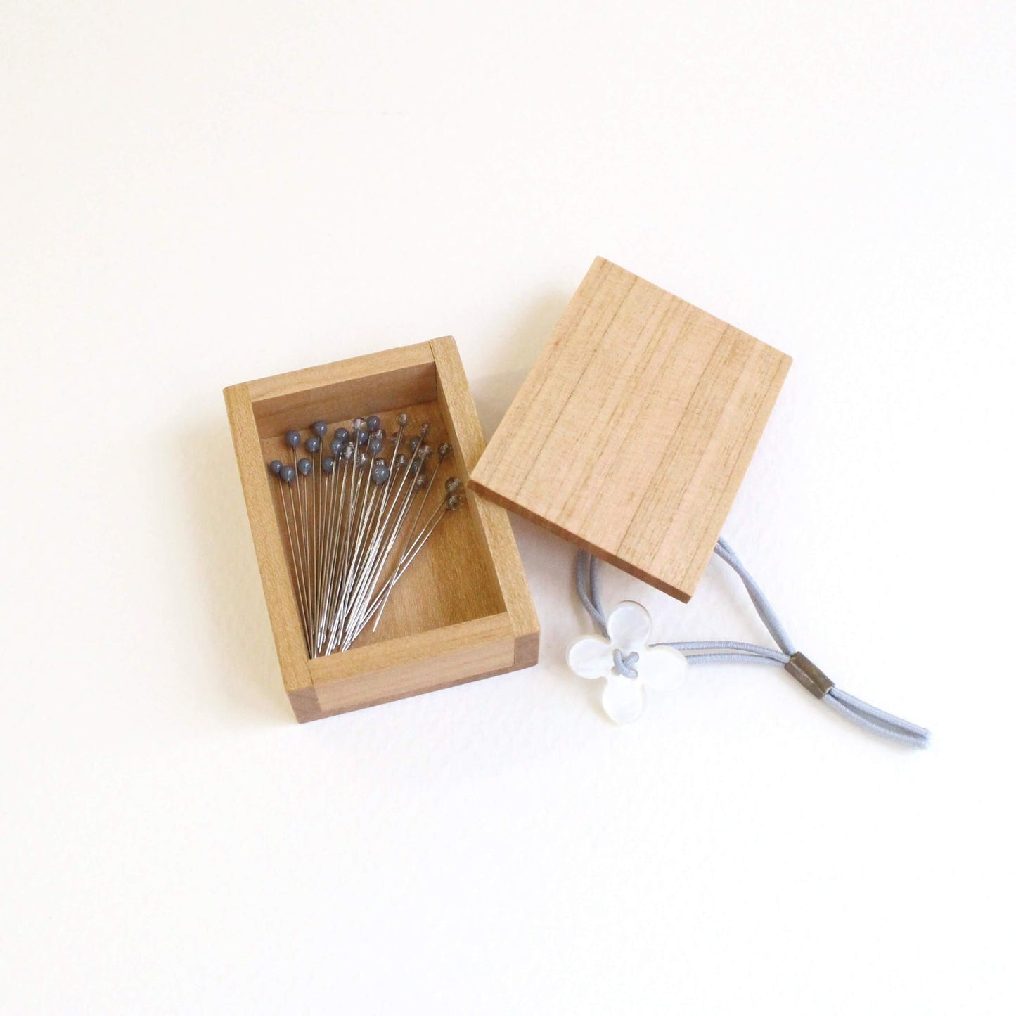 Open wooden box of grey glass headed pins by cohana