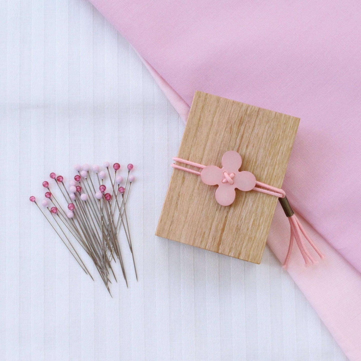 Pink cohana glass headed pins sitting alongside wooden packaging box with pink shell toggle