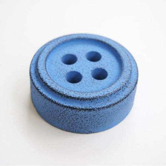 Blue button shaped iron paper weight against white background