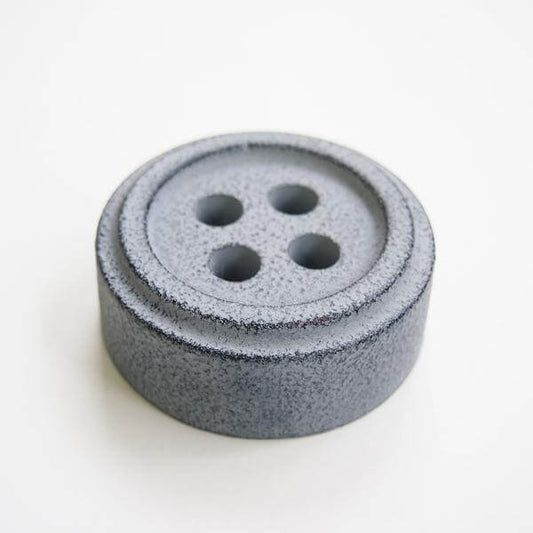 Grey button shaped paperweight against white background