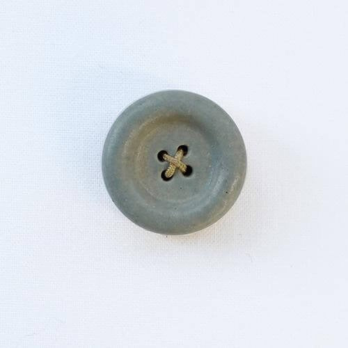 Grey ceramic button shaped needle holder on white background