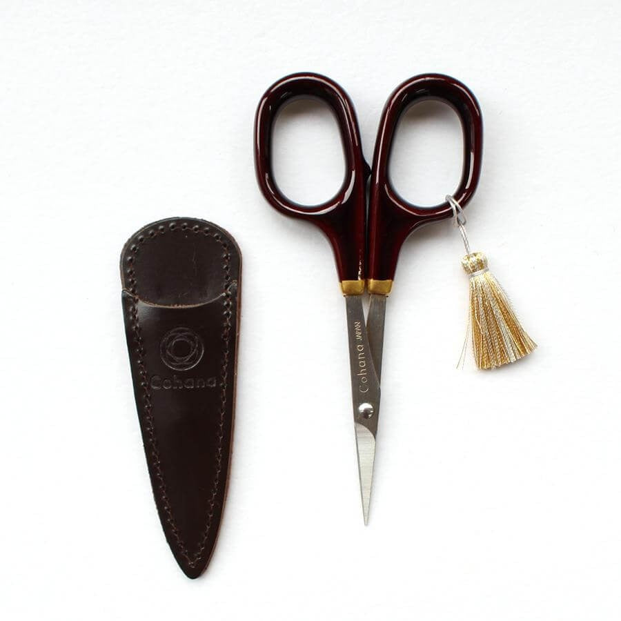 Embroidery scissors with brown lacquer handles and brown leather case on white background
