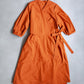 Orange Amalie wrap dress with long sleeves and side bow on a grey background.