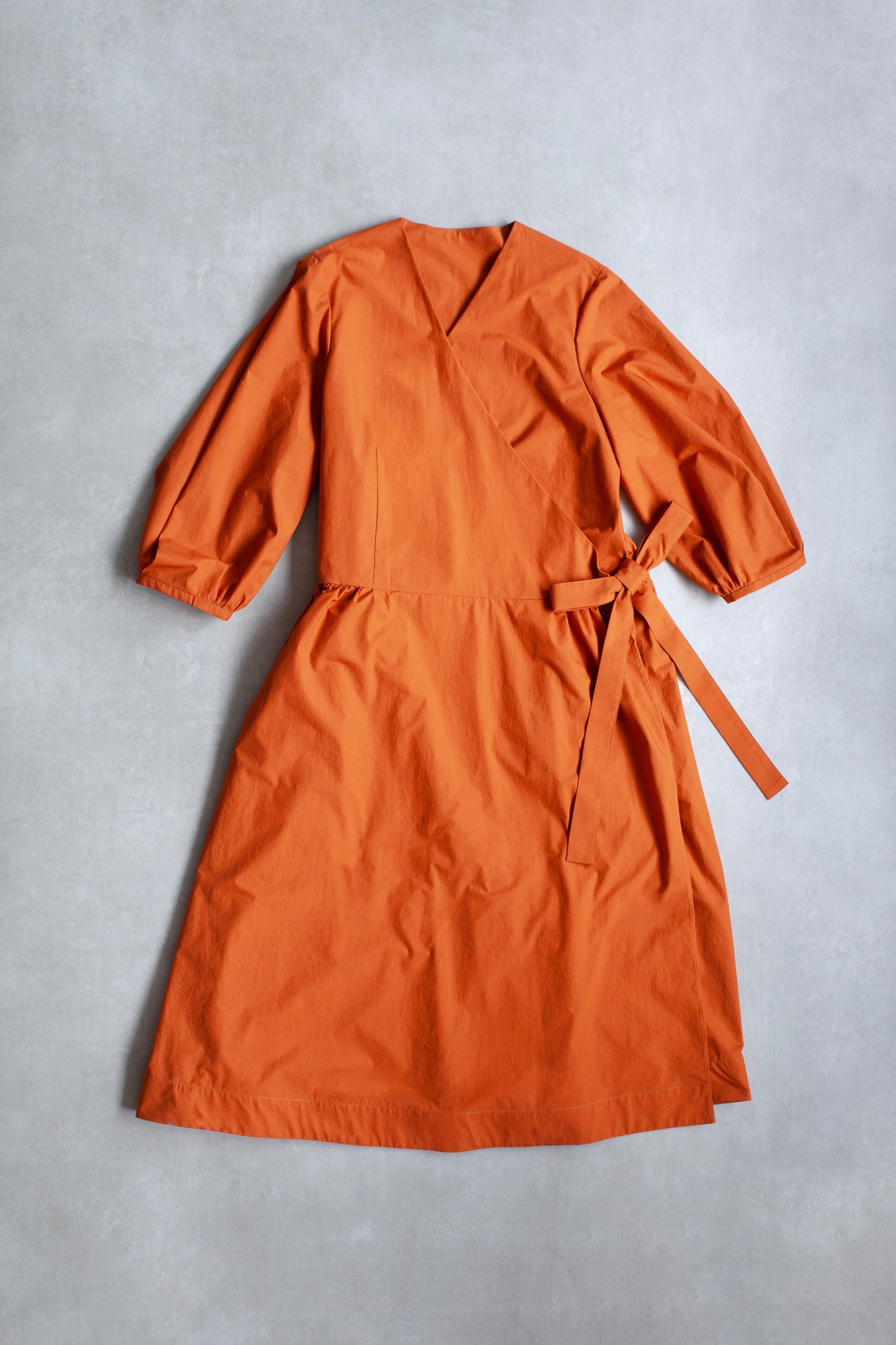 Orange Amalie wrap dress with long sleeves and side bow on a grey background.