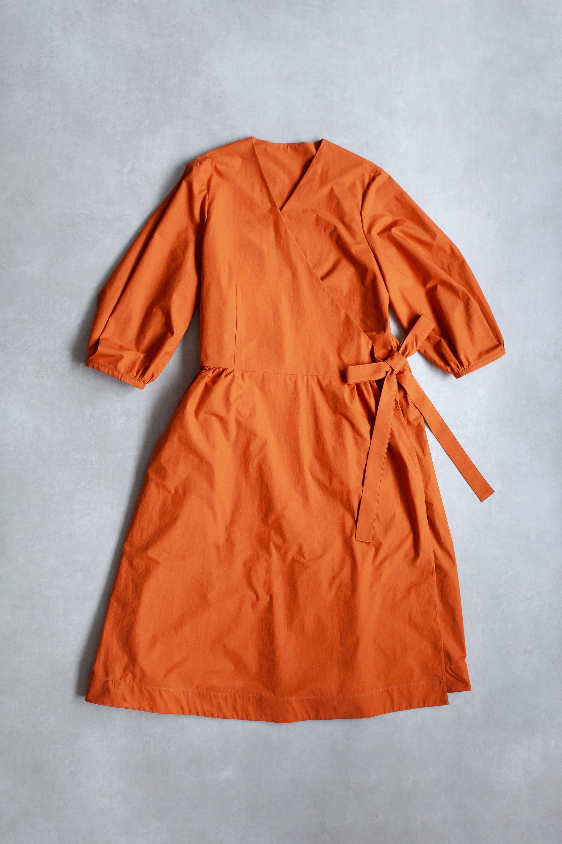 Orange Amalie wrap dress with long sleeves and side bow on a grey background.