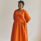 Woman wearing an orange Amalie wrap dress standing against a plain background