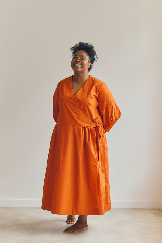 Woman wearing an orange Amalie wrap dress standing against a plain background