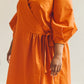 Close up of person wearing an orange Amalie wrap dress against a plain background.