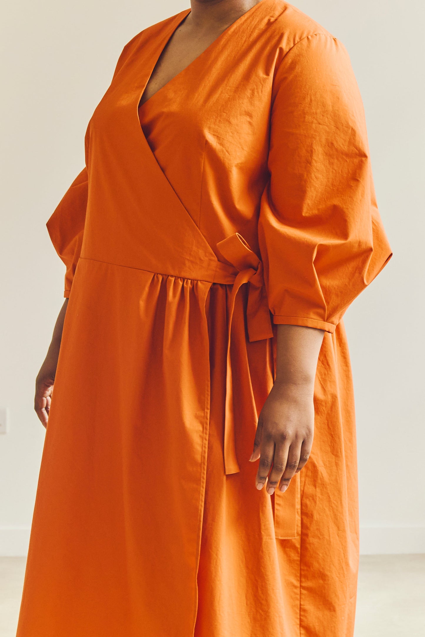 Close up of person wearing an orange Amalie wrap dress against a plain background.