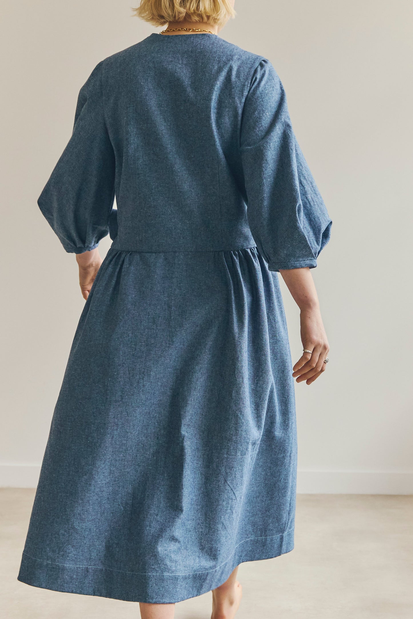 Back view of person wearing a blue Amalie wrap dress with puffed sleeves against a plain background.