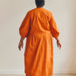 Back view of person wearing an orange wrap dress standing against a plain background