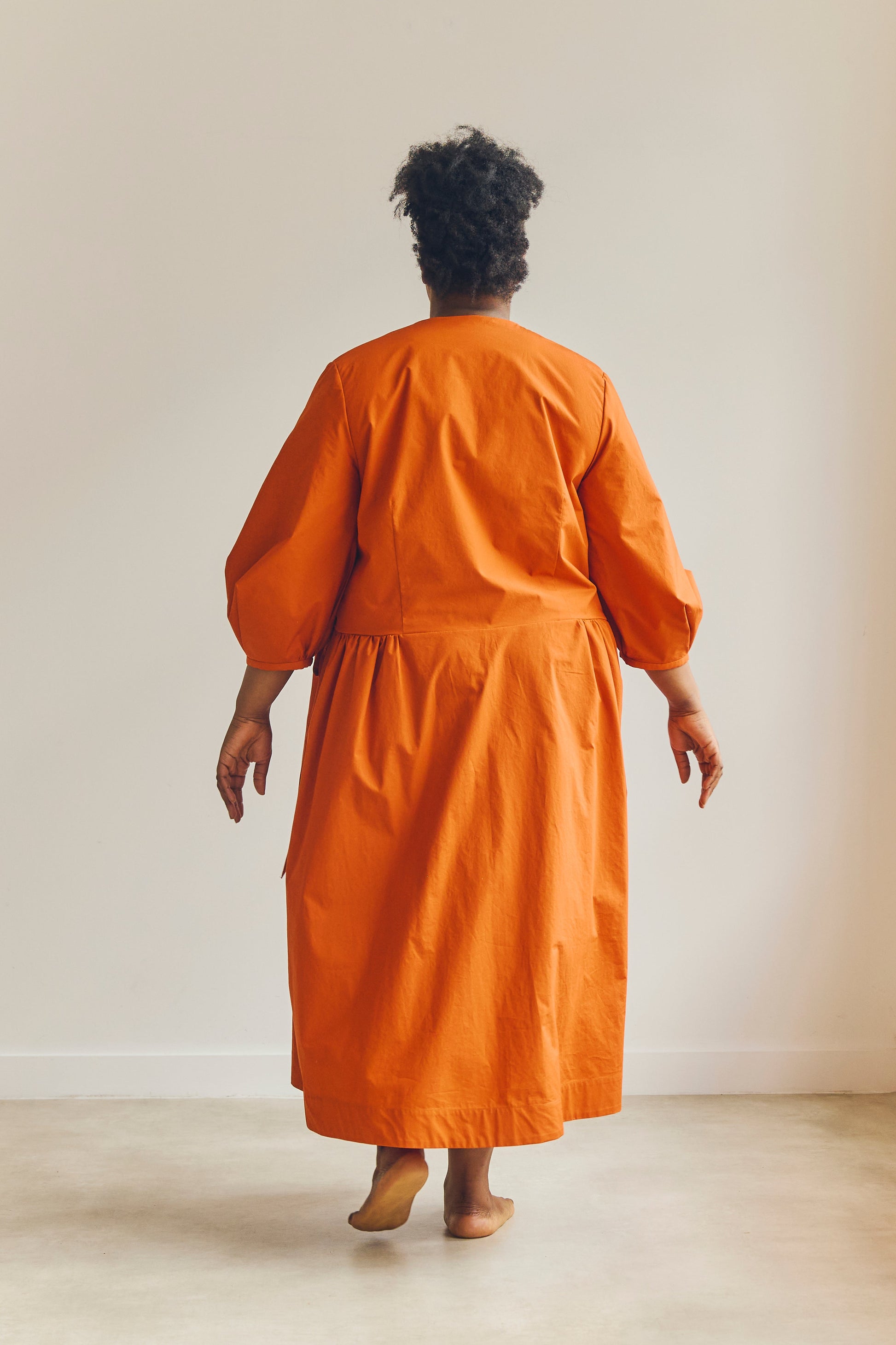 Back view of person wearing an orange wrap dress standing against a plain background