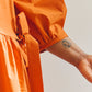 Close up of sleeve detail of person wearing an orange dress with a plain background