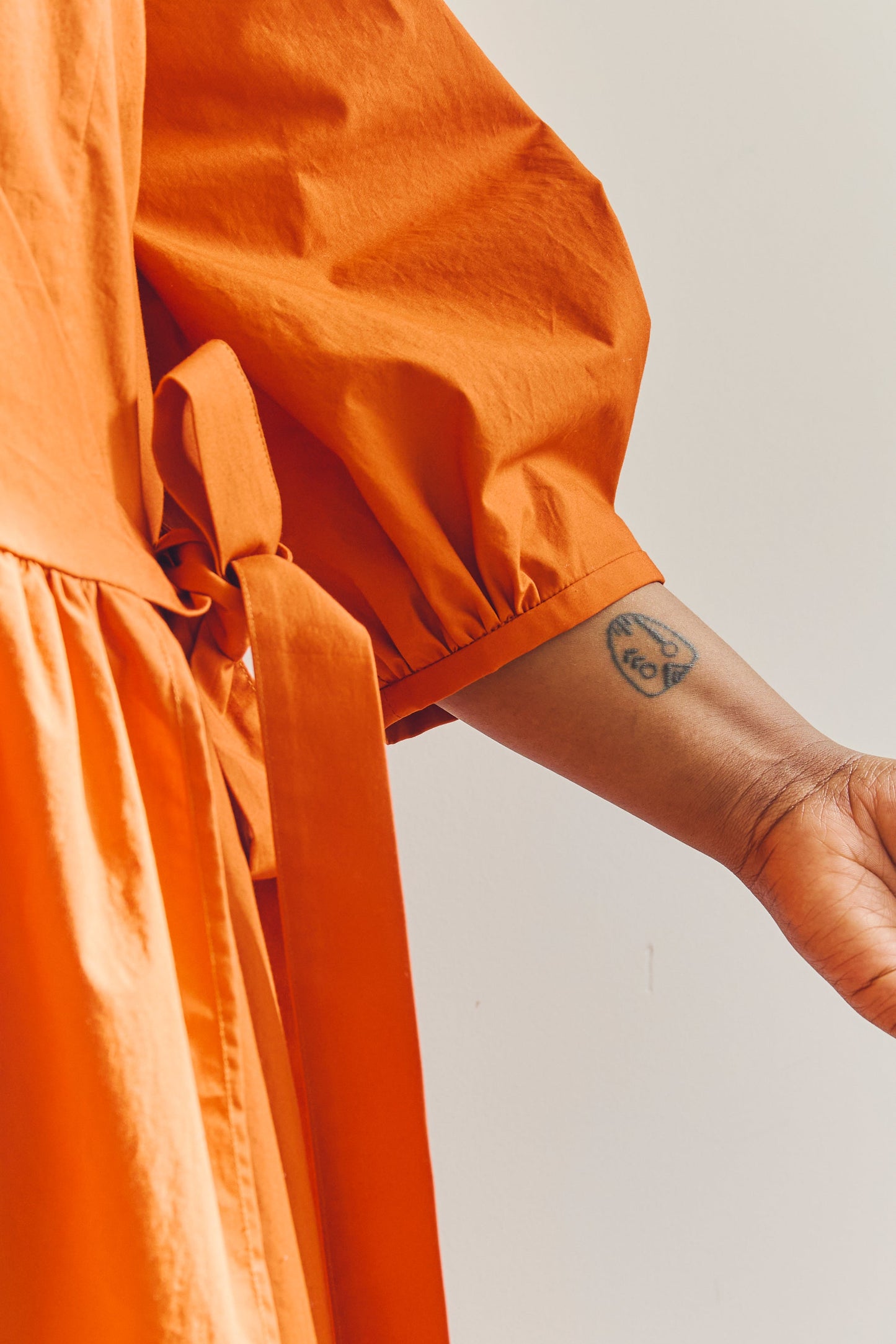 Close up of sleeve detail of person wearing an orange dress with a plain background