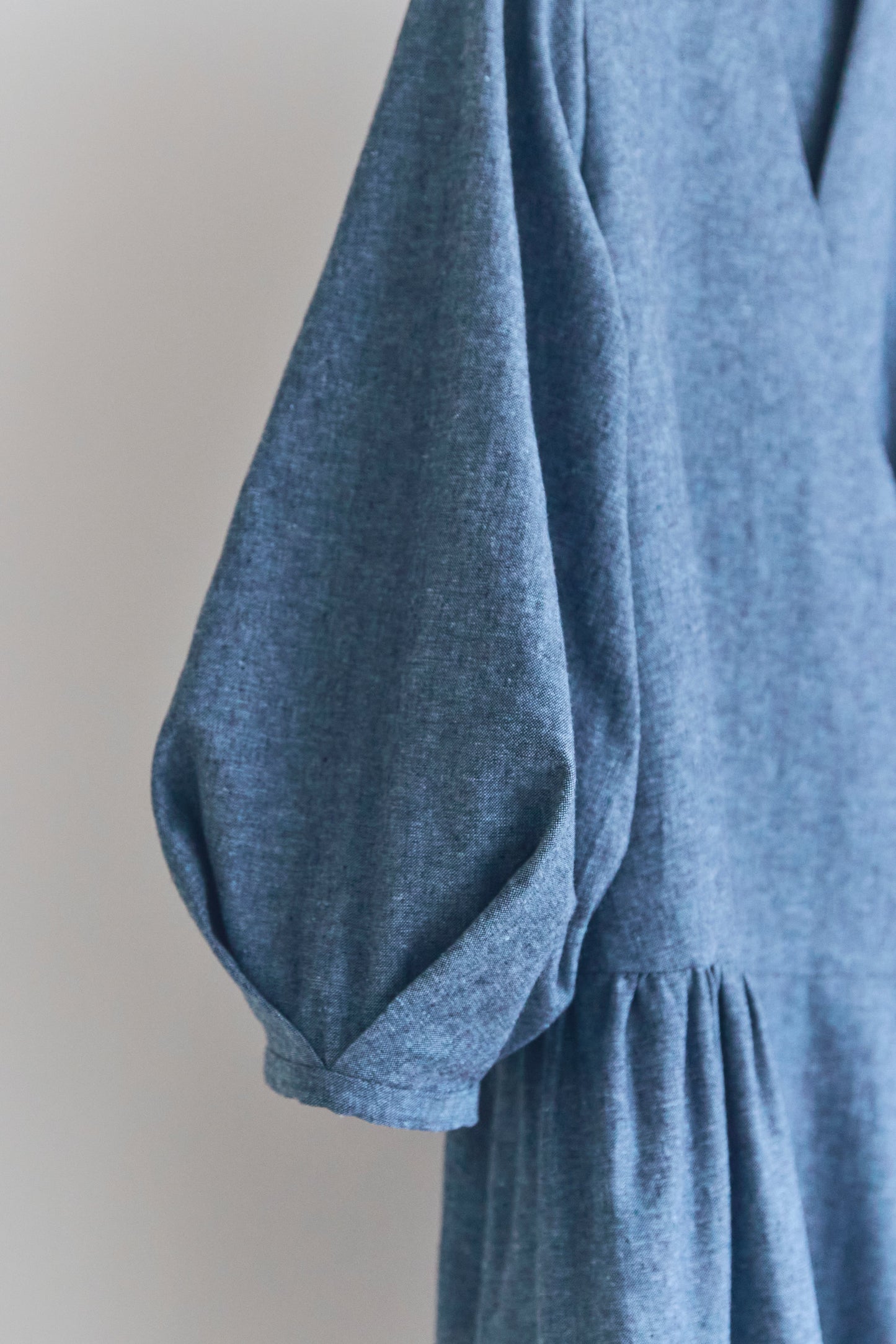 Close up of puffed sleeve of blue dress on a plain background