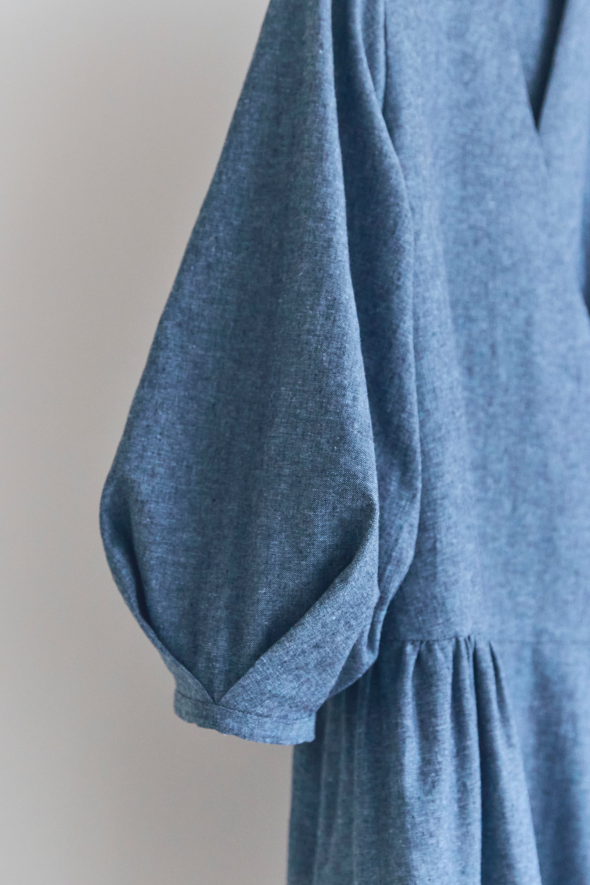 Close up of puffed sleeve of blue dress on a plain background