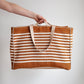 Person holding a striped tote bag against a plain background