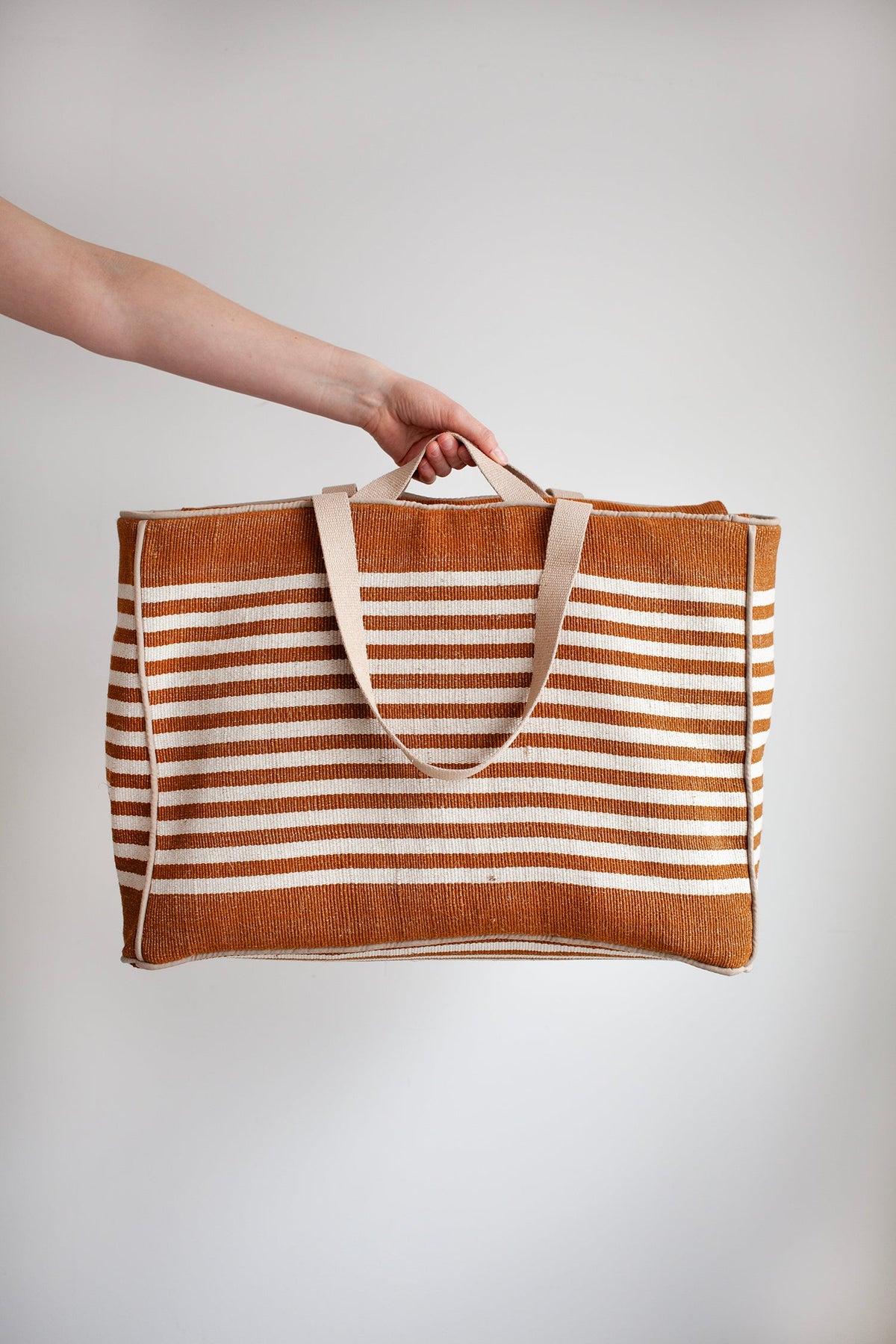 Person holding a striped tote bag against a plain background