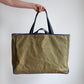 Person holding a green tote bag with black handles against a plain background