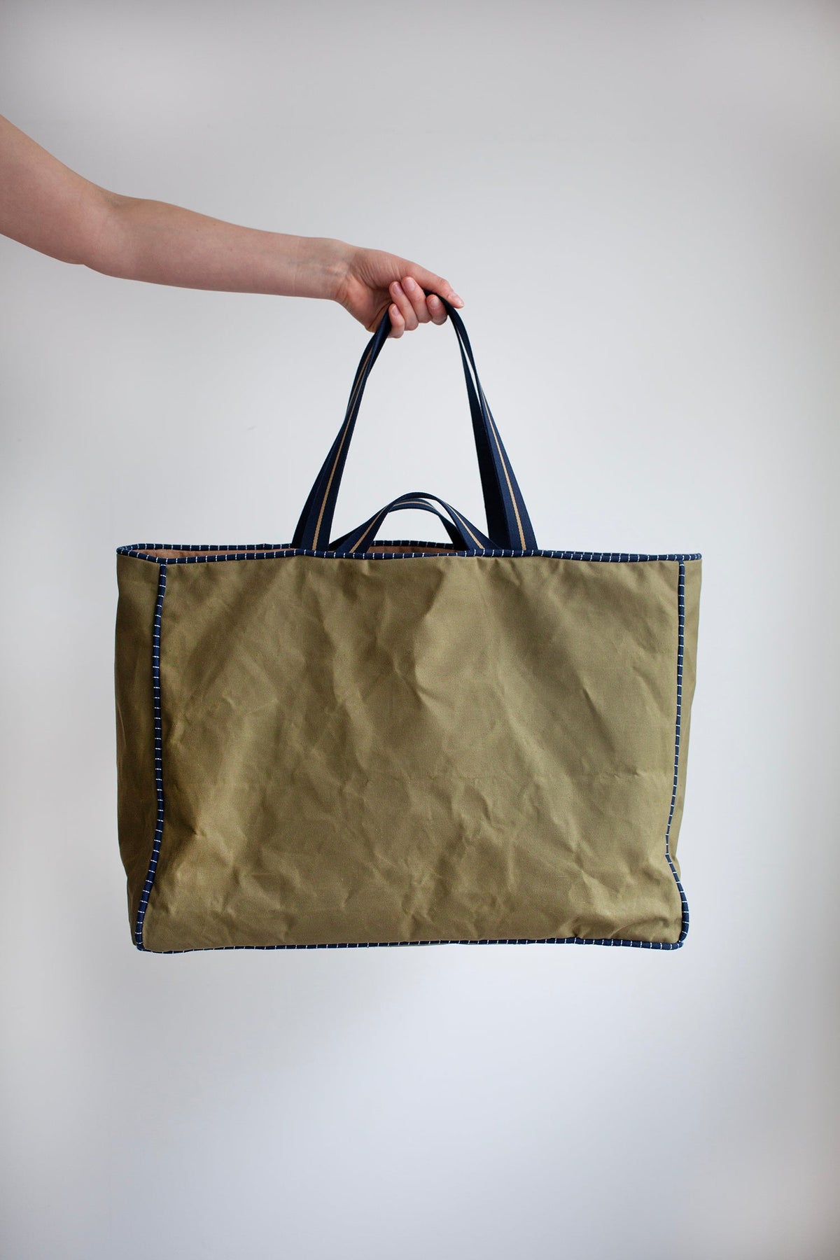 Person holding a green tote bag with black handles against a plain background