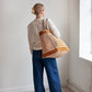 Person holding a striped Away tote bag in a minimalistic room with a window.