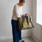 Person holding a green Away tote bag in a minimalistic room with white walls and a radiator.