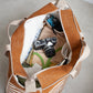 Inside view of brown and beige striped bag with camera and items on a light grey floor.
