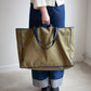 Person holding a large green tote bag against a plain background