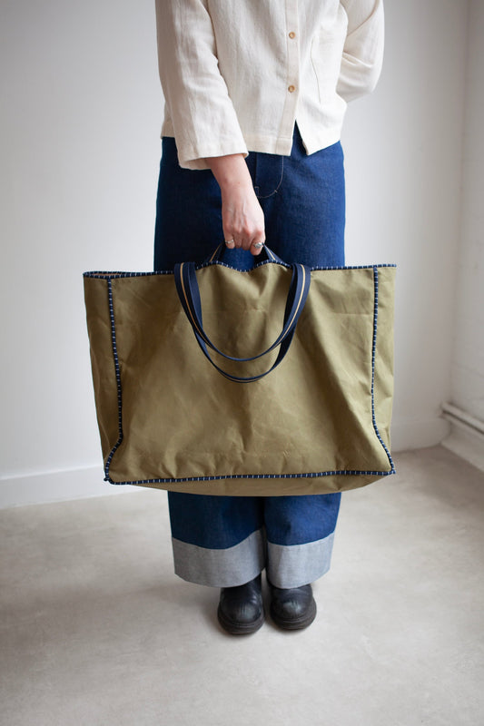 Person holding a large green tote bag against a plain background