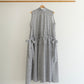 A sleeveless grey and white dress with side tie details, hanging on a wooden hanger from a wooden clothing rack against a plain white wall.