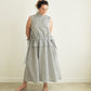 A woman stands barefoot in a minimalist room wearing a sleeveless, high-neck, midi dress with a grey and white pattern.