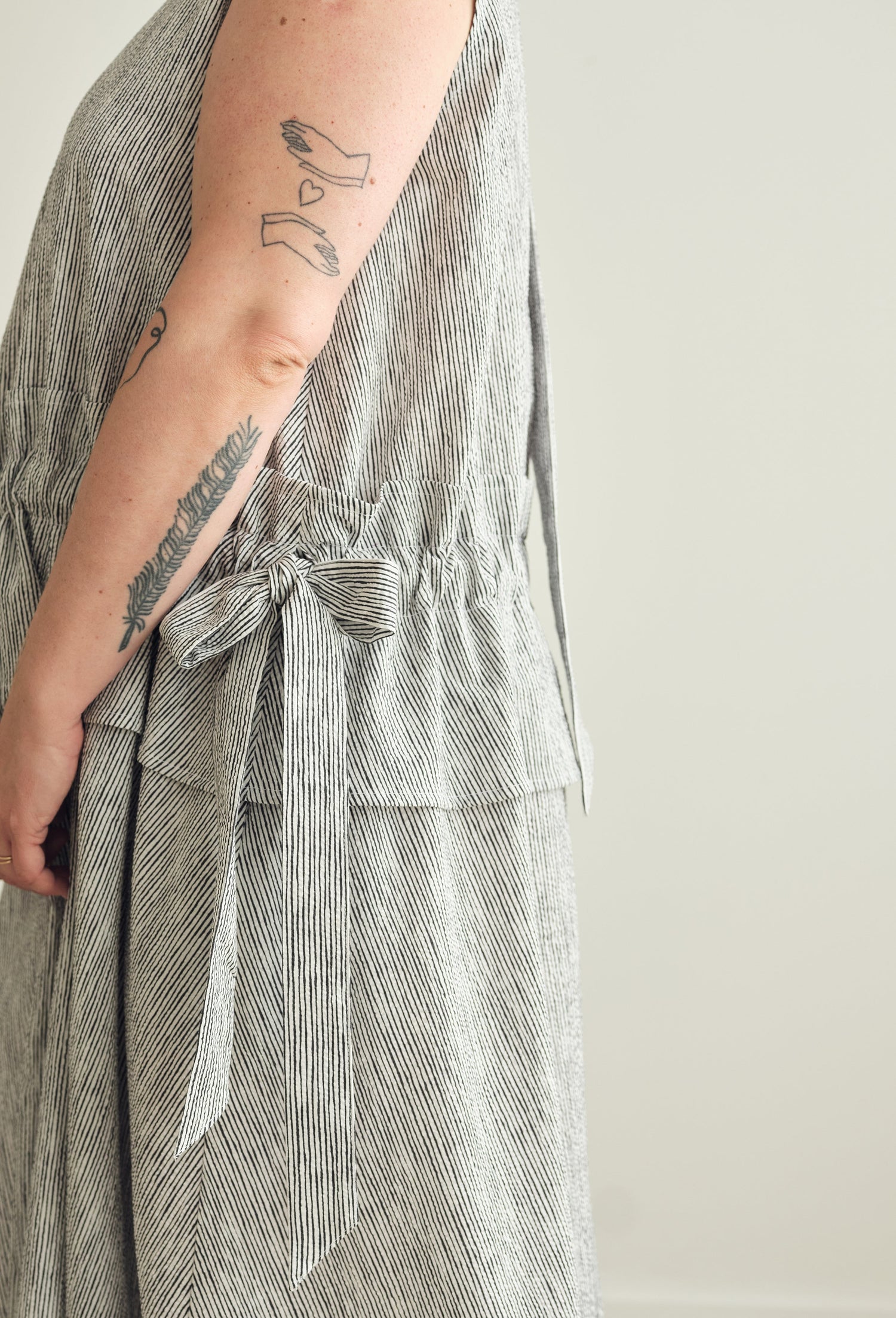 Close up of a person wearing a grey and white striped dress with a white background.