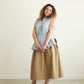 Woman wearing a light blue sleeveless Paloma top and beige skirt against a white background