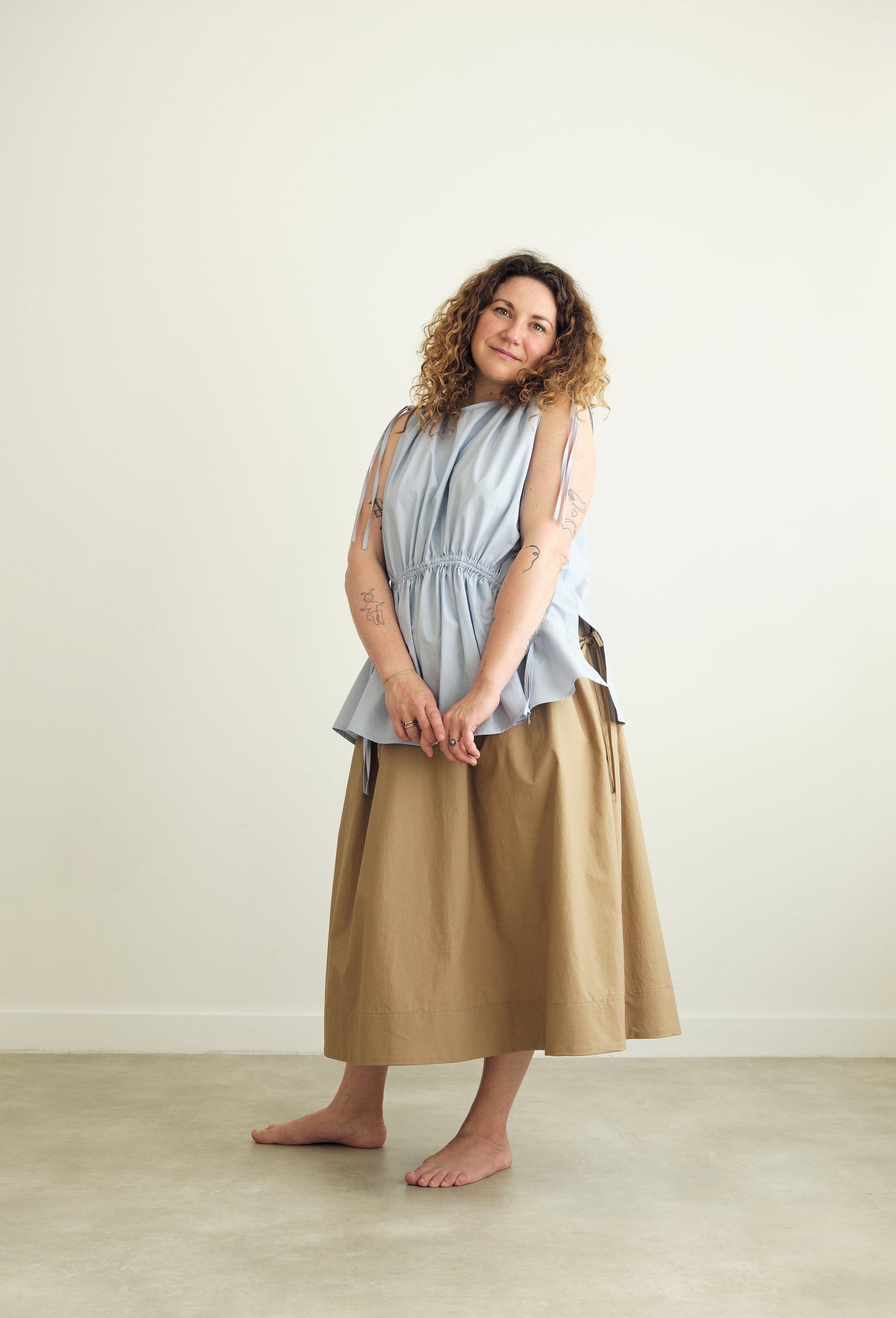 Woman wearing a light blue sleeveless Paloma top and beige skirt against a white background
