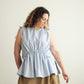 Woman wearing a light blue sleeveless Paloma top and brown skirt against a plain background