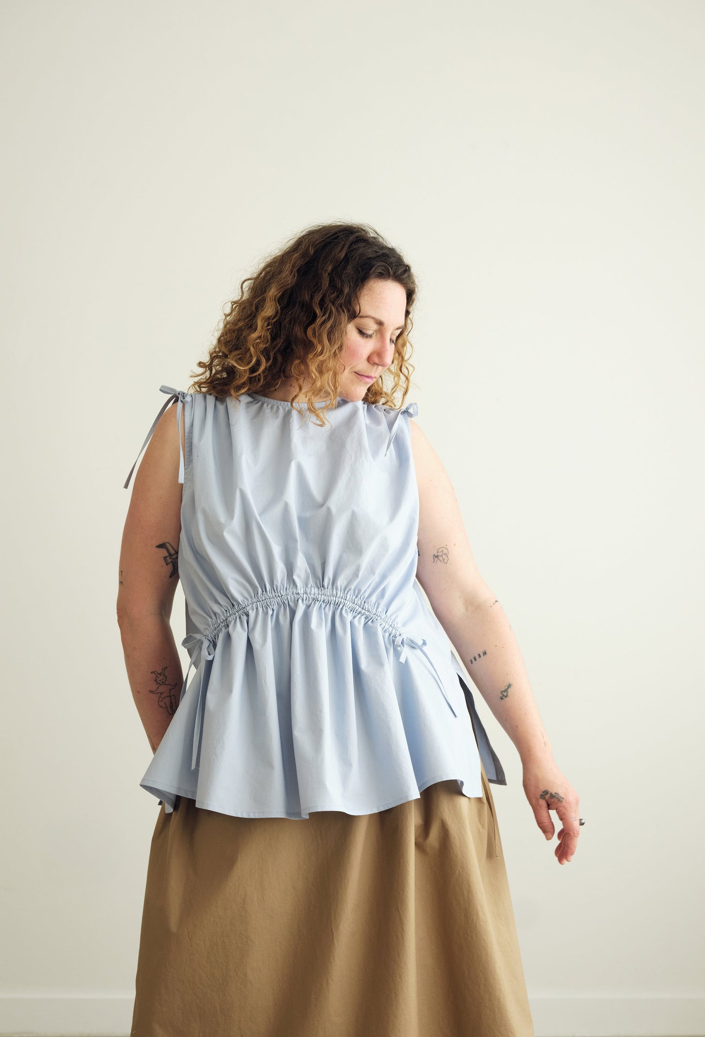 Woman wearing a light blue sleeveless Paloma top and brown skirt against a plain background