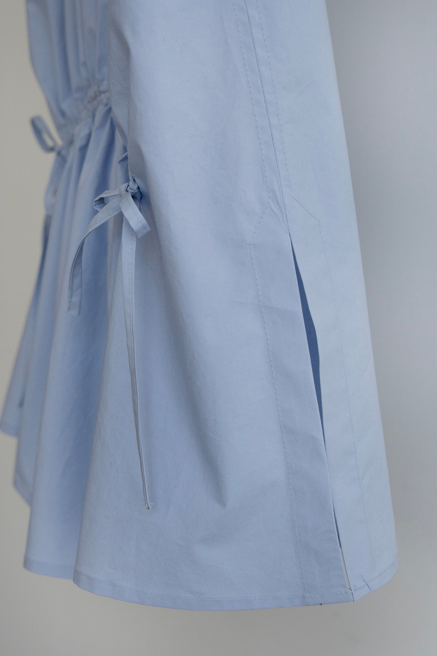 Close-up of a light blue Paloma top, showing side slit detail and matching drawstring tie on a plain light gray background.