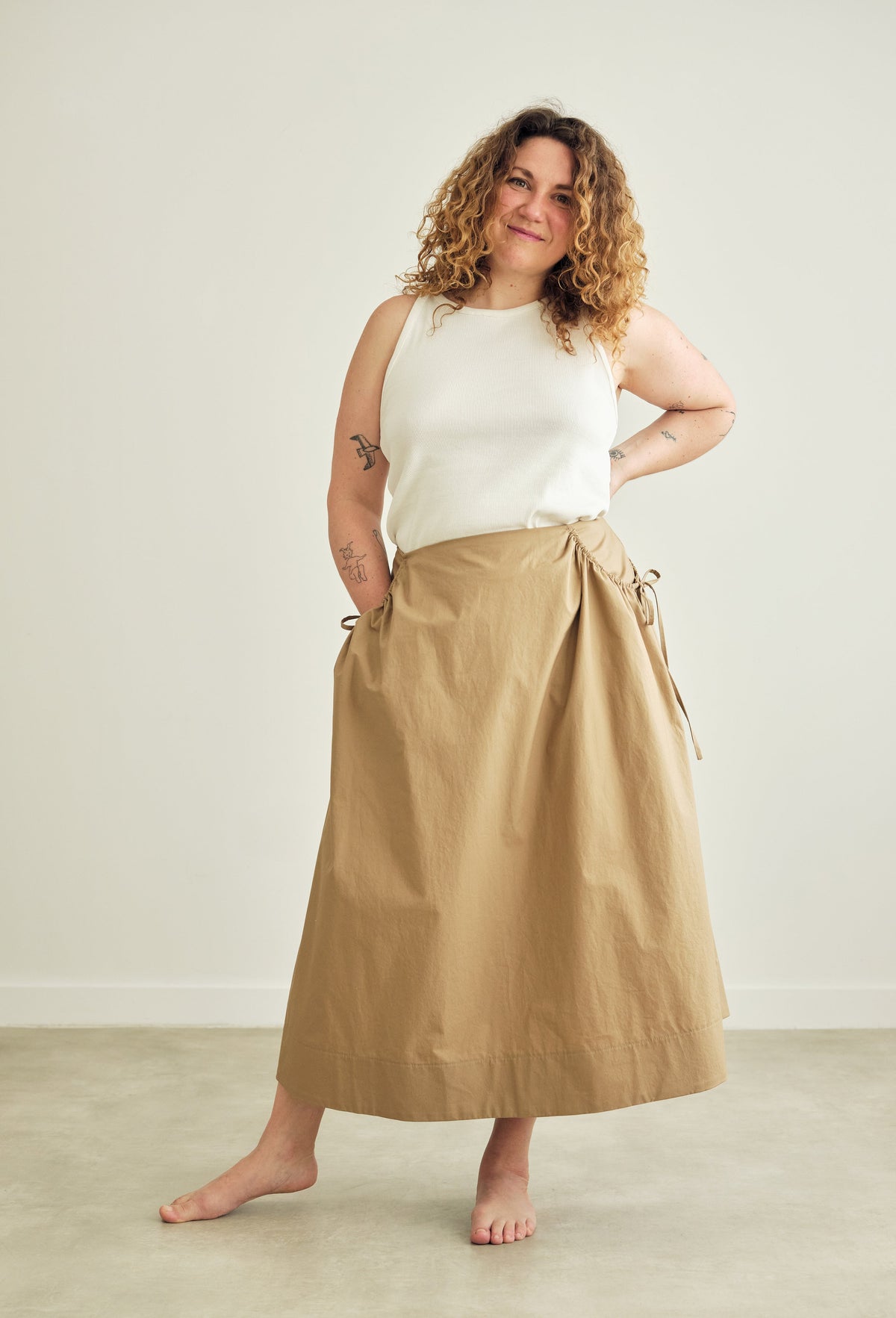 Woman wearing a beige skirt and white top against a plain background